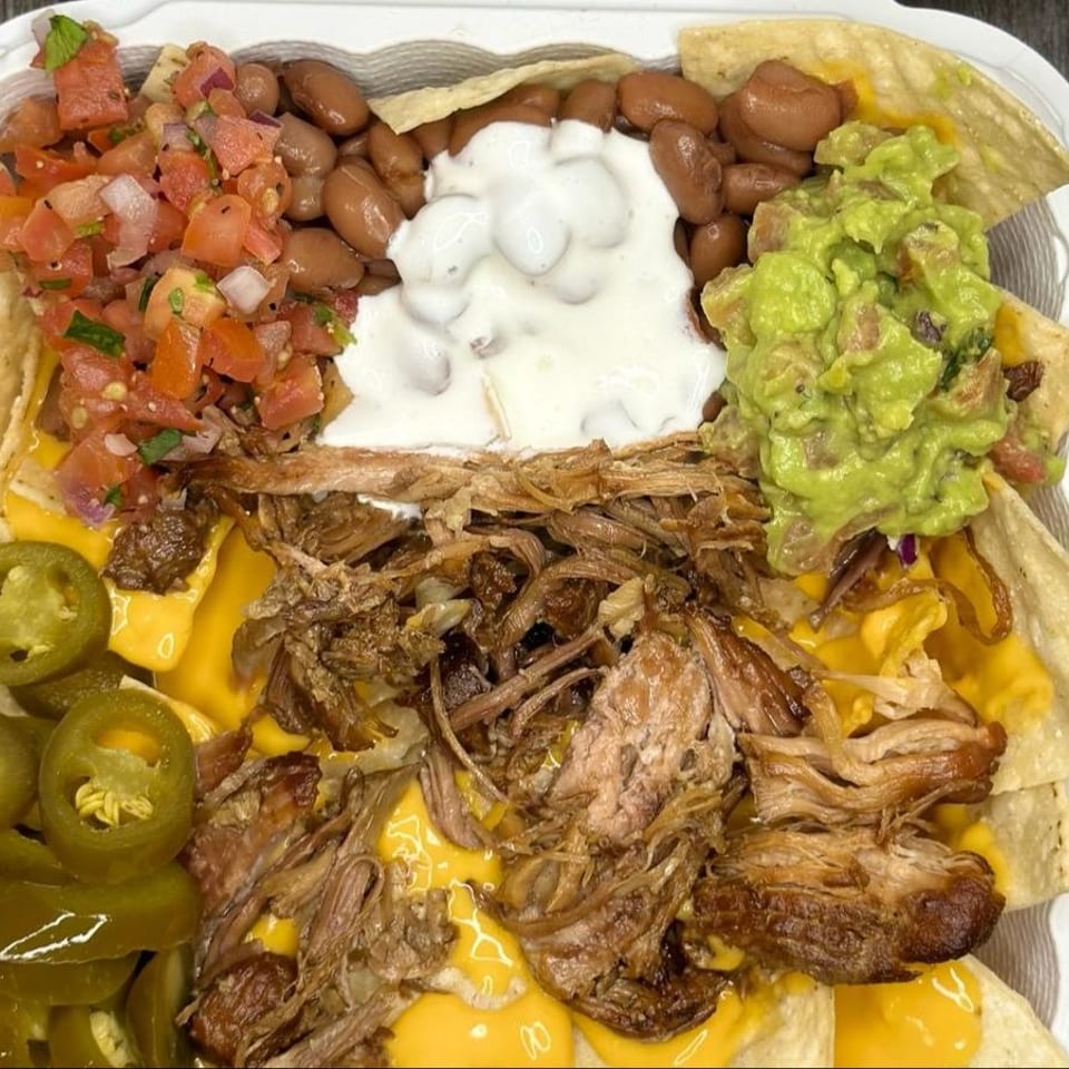 Close-up of loaded nachos with pulled pork, cheese sauce, beans, guacamole, salsa, and jalapeños.