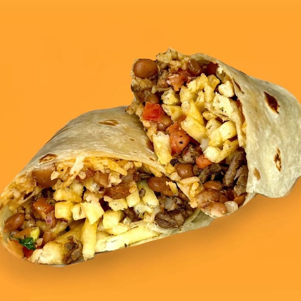 A large burrito, cut in half, revealing a filling of fries, beans, meat, and salsa.