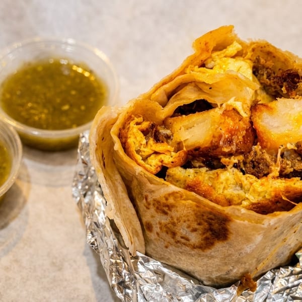 Hearty breakfast burrito filled with eggs, meat, and potatoes, served with two green salsas.
